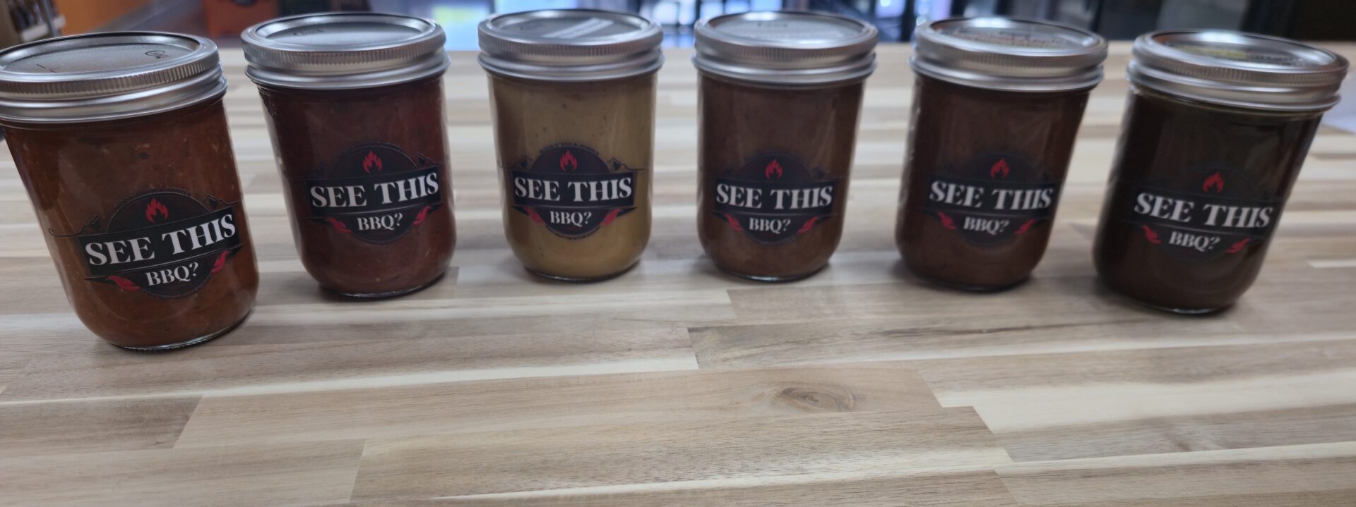 Six jars of BBQ sauce on table.